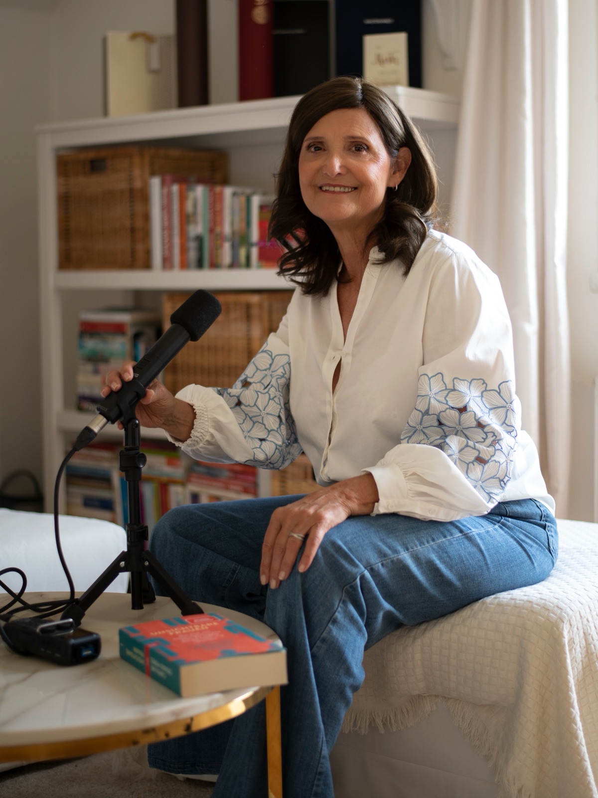 Anita Pitsch in weißer Bluse neben einem Mikrofon, dahinter ein Regal mit Büchern und ihren Studienabschlüssen
